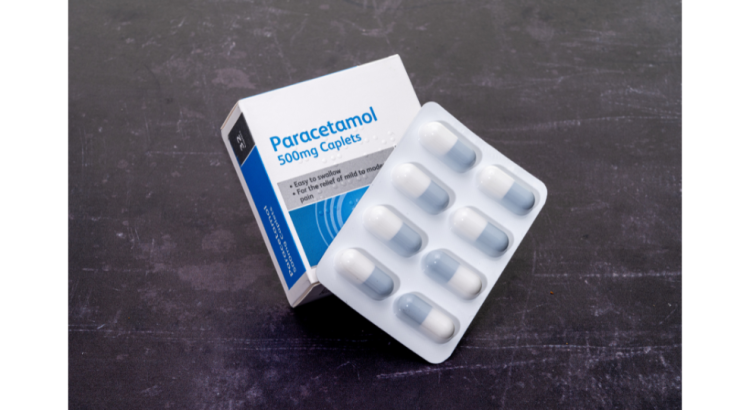 A box of paracetamol on a grey background, with a strip of tablets laying over half of the front of the box