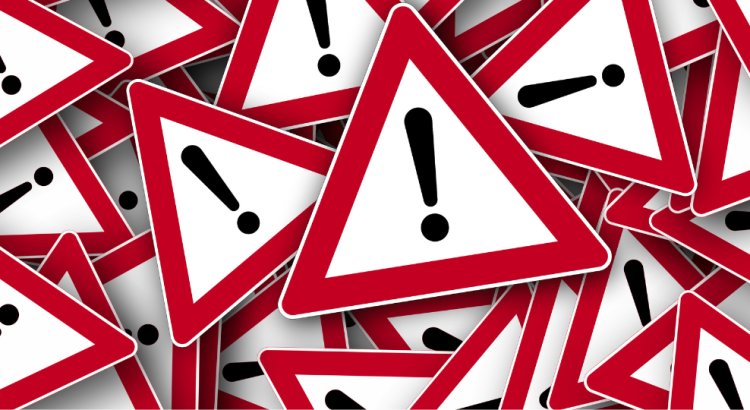 A jumbled pile of triangular alert road signs. The signs are white with a red border and have a black exclamation mark on them