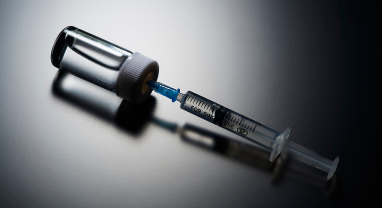 A hypodermic needle and syringe seen against a black shadowy background